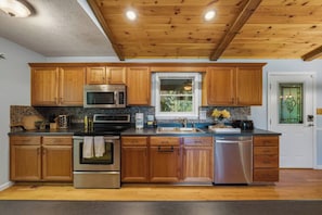 A kitchen with wooden cabinets, stainless steel appliances, a window, and a door with a stained glass design. - 5BR Smoky Mountain Escape, Hot Tub, Game Room, Sleeps 14,  10 min to Dollywood (Pigeon Forge)