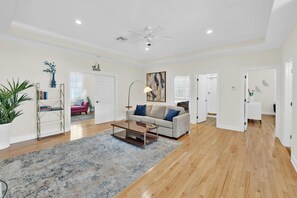 A spacious living room with hardwood flooring, a beige sofa, a coffee table, and a ceiling fan. - Bay Breeze Retreat | 6BR Group Getaway | Sleeps 15. (Panama City)