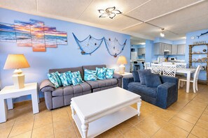 A living room with a sofa, two side tables, a coffee table, and a dining area with a table and chairs. - Atlantis 1403 (Ocean City)