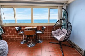 A dining area with a table and chairs, a hanging chair, and a view of the sea through large windows. - Atlantis 1403 (Ocean City)