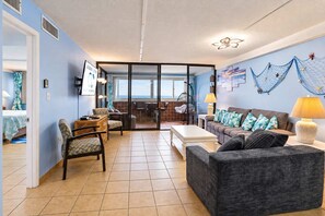 A spacious living room with a sofa, chairs, a coffee table, and a view through a glass door to the outside. - Atlantis 1403 (Ocean City)