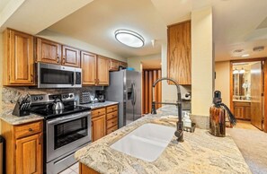 A kitchen with wooden cabinets, stainless steel appliances, granite countertops, and a modern faucet. - Torian Plum Cozy 1-bedroom condo with AC Ski in/Ski Out Steamboat Springs (Steamboat Springs)