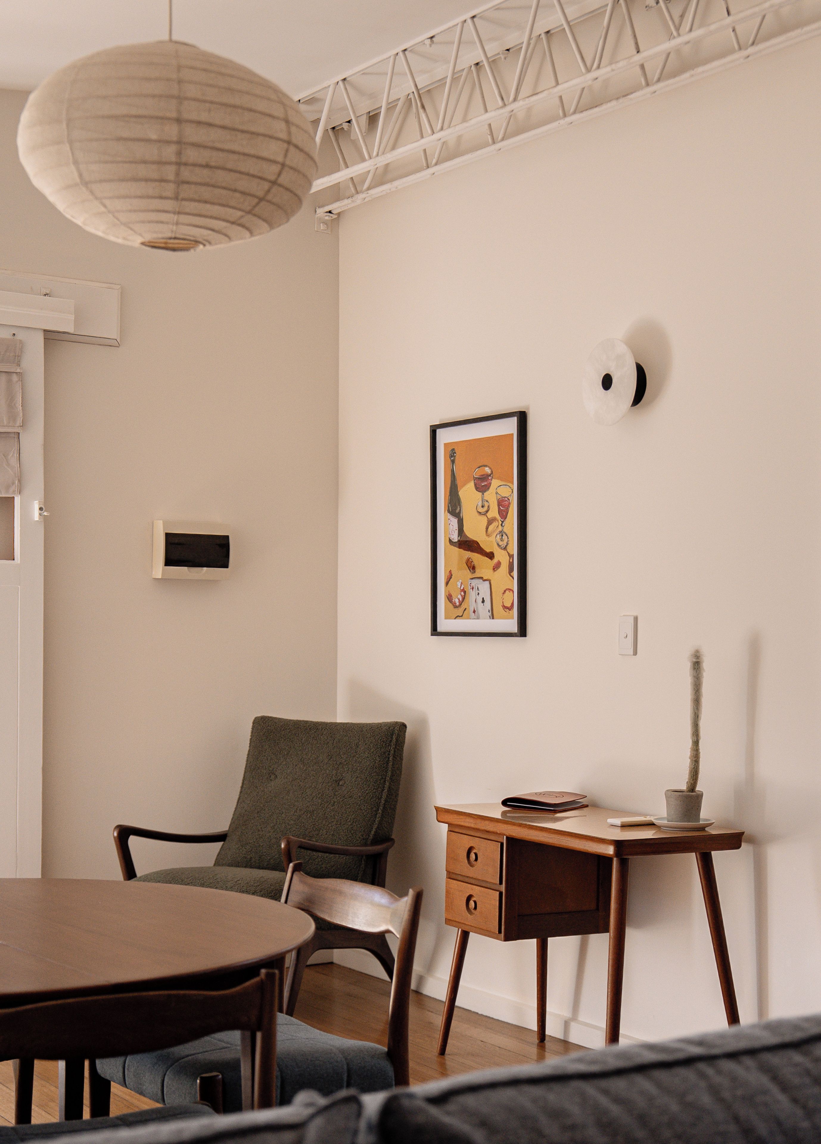 A room with a dining table, a chair, a desk with drawers, a hanging light fixture, and a framed picture on the wall.