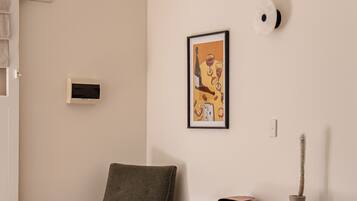 A room with a dining table, a chair, a desk with drawers, a hanging light fixture, and a framed picture on the wall.