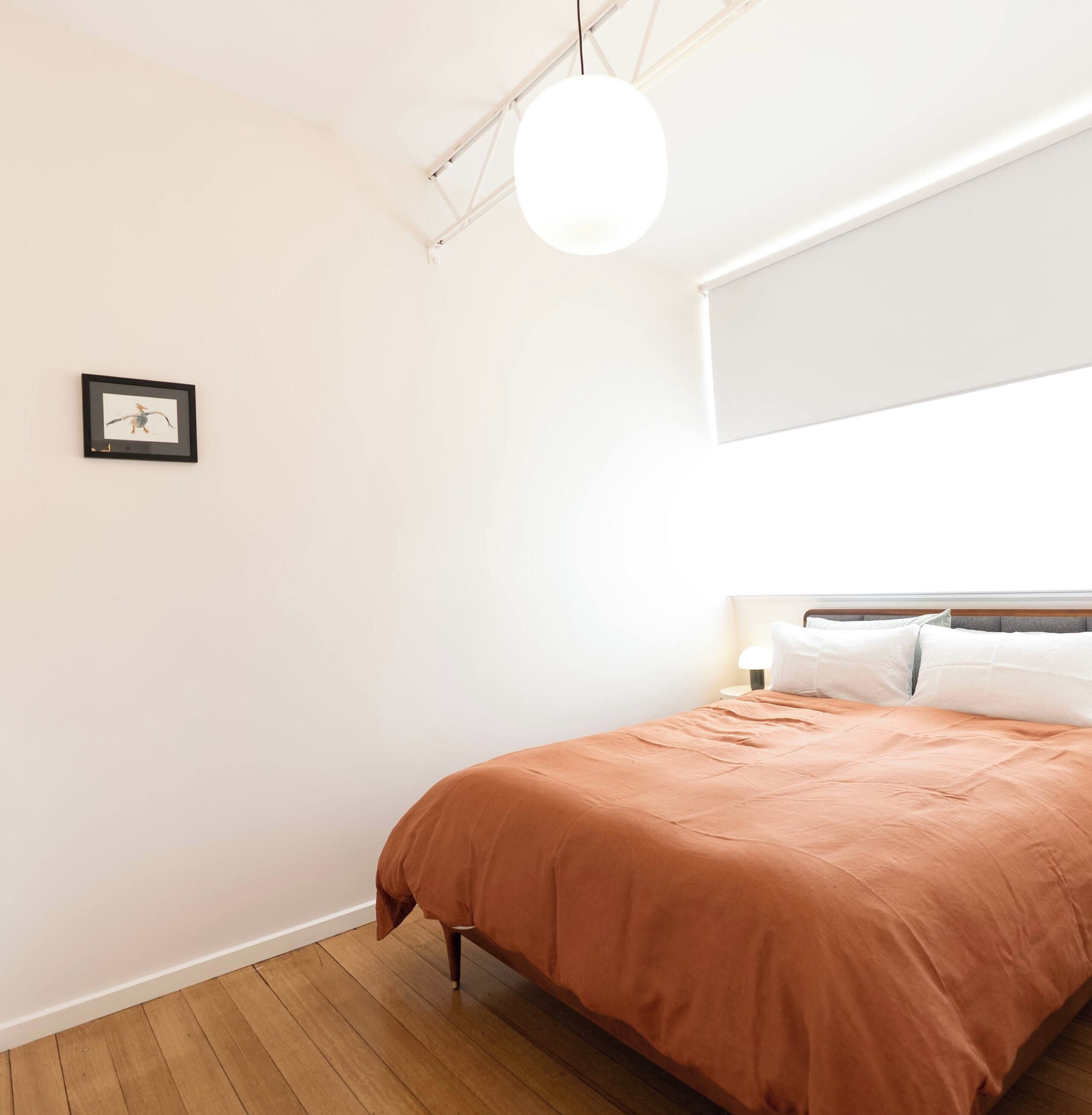 Une chambre à coucher avec un lit, un luminaire suspendu et un tableau encadré au mur.