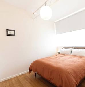A bedroom with a bed, a hanging light fixture, and a framed picture on the wall.