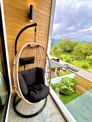 A hanging chair with a black cushion in a room with a wooden wall and a window overlooking a green landscape. - Blue Lion Villa Private Pool 3BR Kamala (Kamala)