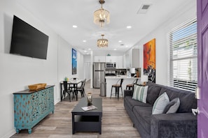 A modern living room with a sofa, a coffee table, and a dining area with chairs. - 3BR, 2 Bath NOLA Home w/ Patio (New Orleans)