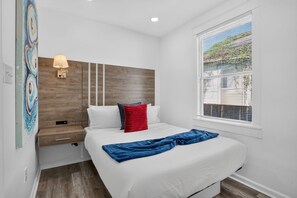 Un dormitorio con cama, mesita de noche, lámpara y ventana con persianas.