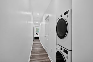 A laundry room with a washing machine and dryer, a wooden floor, and a door leading to a bedroom. - 3BR, 2 Bath NOLA Home w/ Patio (New Orleans)