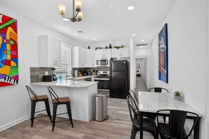 A modern kitchen with white cabinets, a black refrigerator, and a dining area with a white table and black chairs. - Colorful New Orleans Home 3BR Near French Quarter (New Orleans)