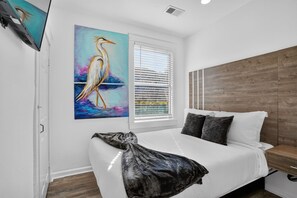 A bedroom with a bed, a painting of a bird, a window with blinds, and a wooden headboard. - Colorful New Orleans Home 3BR Near French Quarter (New Orleans)