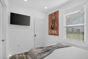 A bedroom with a bed, a television mounted on the wall, a door, and a window with blinds. - Colorful New Orleans Home 3BR Near French Quarter (New Orleans)