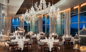 A restaurant with multiple tables, chandeliers, and a piano. - Vidanta Vallarta Luxury-Grand Luxxe Junior Suite-Premier Golf, Spa, Beach (Las Jarretaderas)