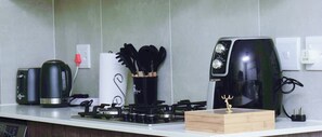 A kitchen with a coffee maker, a kettle, a toaster, a stove, and a wooden box on the counter. - Royal Golfview Stay  - Welcoming luxury 1-bedroom Apartment near OR Tambo (Boksburg)
