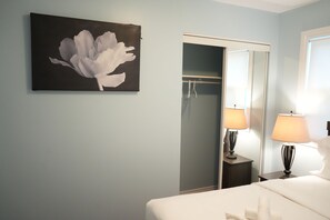 A hotel room with a bed, a nightstand with a lamp, a wardrobe, and a painting of a flower on the wall.