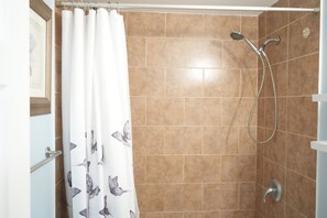 A shower area with a showerhead and hose, a white curtain with a butterfly pattern, and a tiled wall.