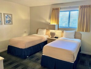A hotel room with two beds, a bedside table with a lamp, and a window with curtains. - Las Olas Beach Club (Satellite Beach)