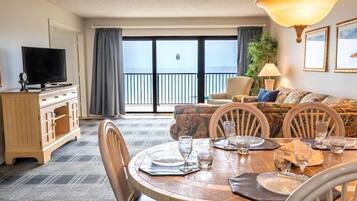 A hotel room with a dining area, a television, a sofa, and a balcony with a view.