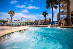 Una piscina con sillones de descanso y palmeras.