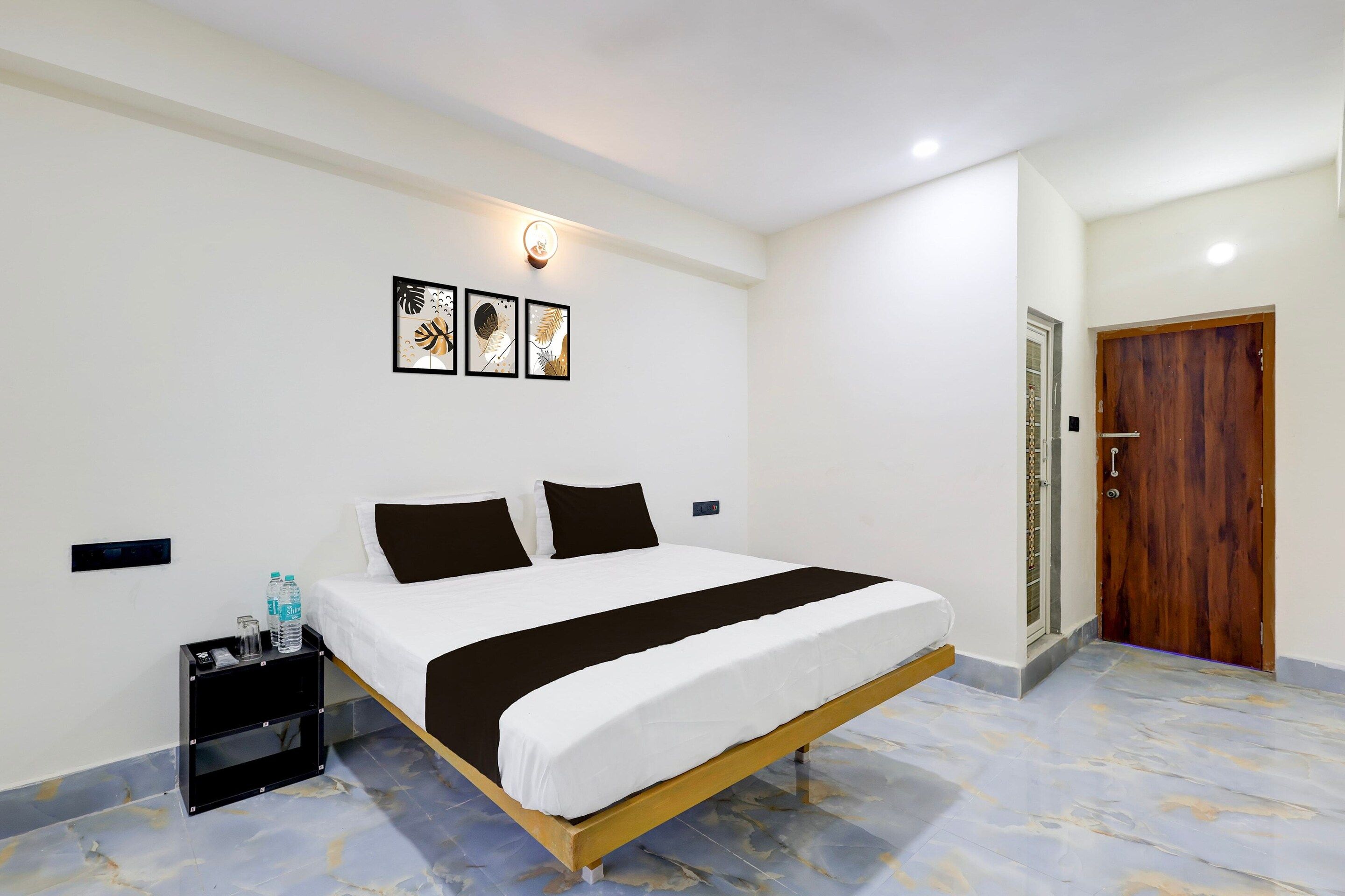A hotel room with a bed, a nightstand, a wall-mounted light, and a door.