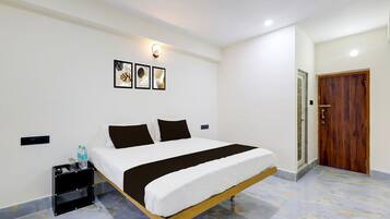 A hotel room with a bed, a nightstand, a wall-mounted light, and a door.