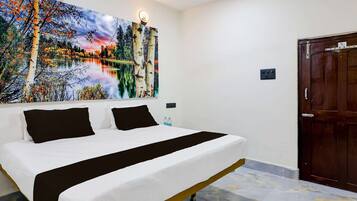 Quarto de hotel com cama, uma grande pintura de paisagem, uma porta e uma tomada.