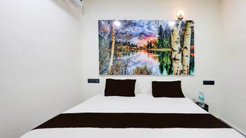 A hotel room with a bed, a nightstand, a wall-mounted painting of a landscape, and a wall-mounted light.