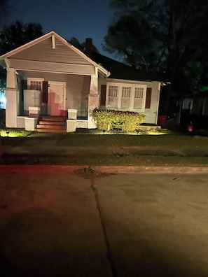 A two-story house with a front porch, a visible garage door, and a small front yard with a bush. - Cozy 2-bedroom bungalow near Mercer in Macon with AC (Macon)