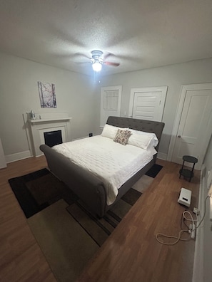A bedroom with a bed, a ceiling fan, a fireplace, and a small table. - Cozy 2-bedroom bungalow near Mercer in Macon with AC (Macon)