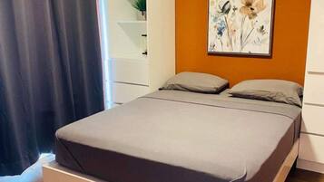 Ein Schlafzimmer mit einem Bett, einem Bild an der Wand und einem Fenster mit Vorhängen.