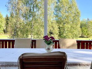 A dining table with a vase of flowers, surrounded by chairs, set outdoors with a view of trees. - 7 Person Holiday Home in Graddo (Gräddö)