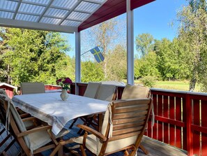 An outdoor patio with a table and chairs, a flag, and a view of trees and a field. - 7 Person Holiday Home in Graddo (Gräddö)