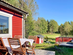 A red building with a porch, outdoor seating, and a view of a green landscape. - 7 Person Holiday Home in Graddo (Gräddö)