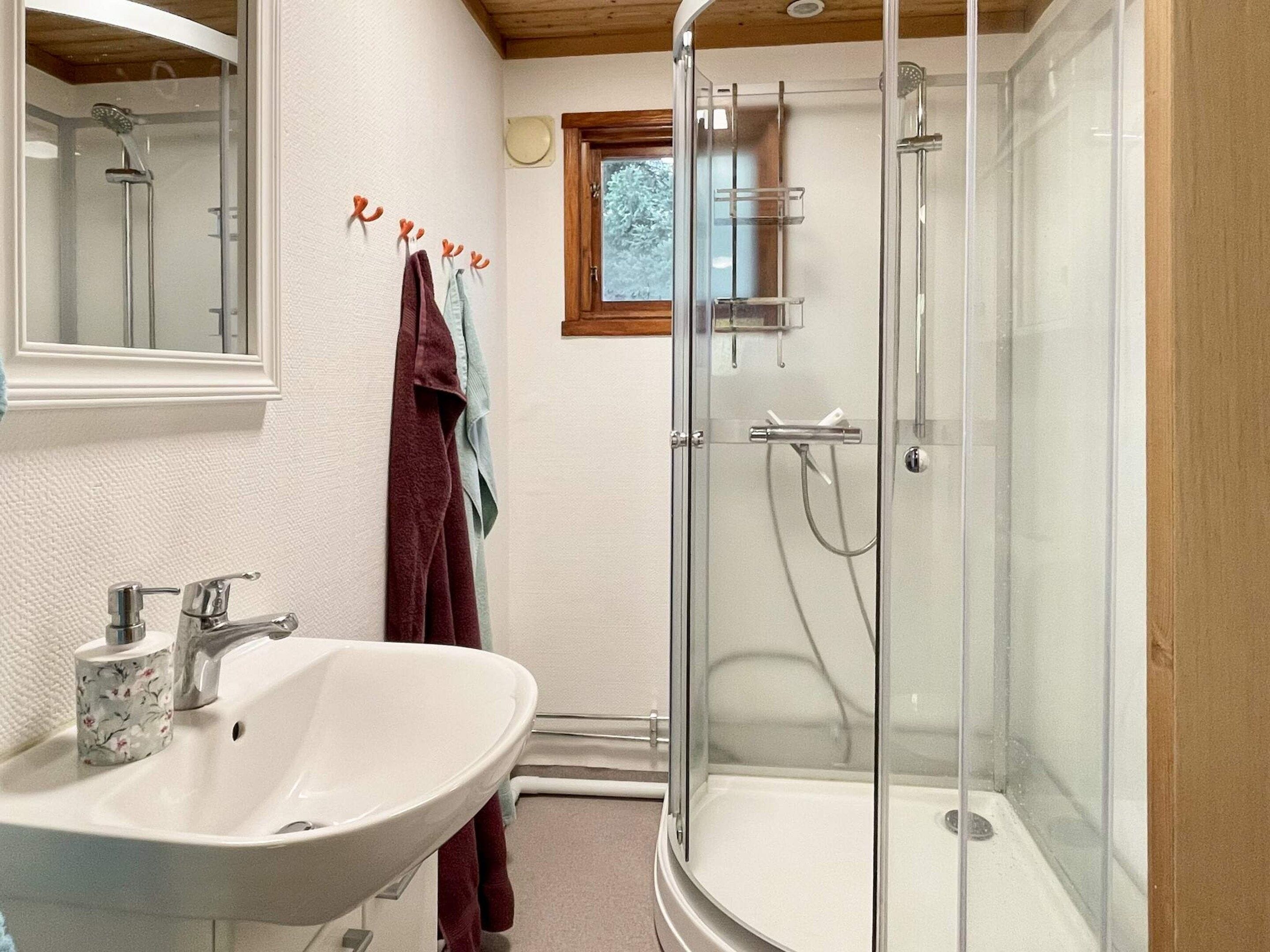 A bathroom with a glass-enclosed shower, a white sink with a floral soap dispenser, and a wooden ceiling.