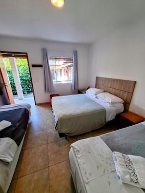 A hotel room with two beds, a window with curtains, and a view of greenery outside. - Vila Palmar Hospedagem (Vassouras)