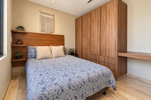 A bedroom with a bed, wooden wardrobe, bedside tables, and a wall-mounted macrame piece. - 2 BR Penthouse, Downtown area, Ocean views (Cabo San Lucas)