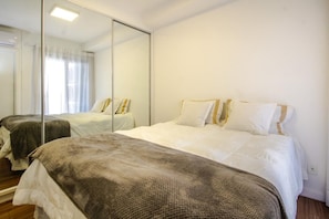 A hotel room with a large mirror, a bed with white bedding, and a bedside table. - Habitarte | 2 suites with views and leisure facilities high up (São Paulo)