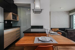 A modern kitchen with a dining area, featuring a built-in microwave, a large island, and a seating arrangement with a sofa and chairs. - Habitarte | 2 suites with views and leisure facilities high up (São Paulo)