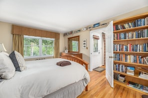 Une chambre à coucher avec un grand lit, une commode en bois, une bibliothèque et une porte donnant sur une autre pièce.