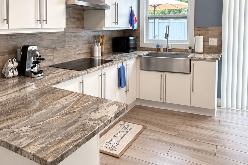Eine moderne Küche mit Marmorarbeitsplatte, Edelstahlspüle und weißen Schränken.