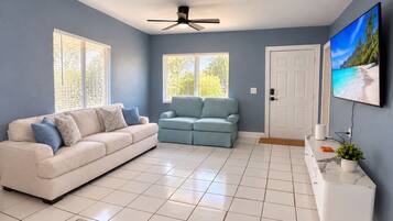 A living room with a beige sofa, a blue sofa, a white TV stand, and a ceiling fan.