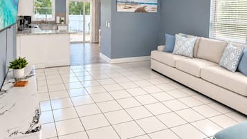 A modern living room with a sofa, a television, and a kitchen area in the background.