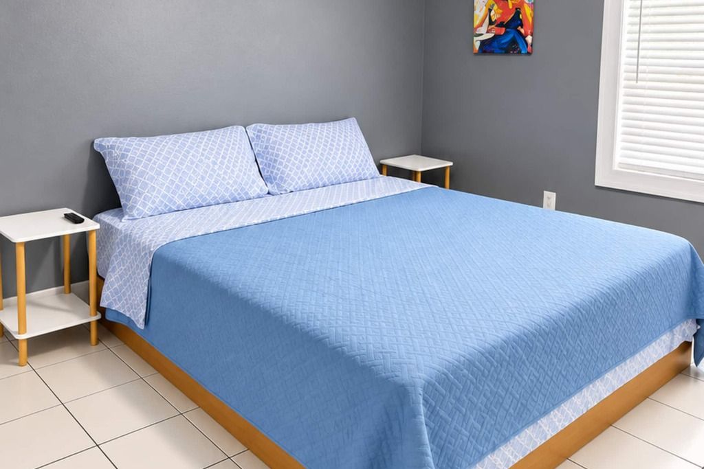A bed with a blue quilt, two bedside tables, and a wall with a painting.
