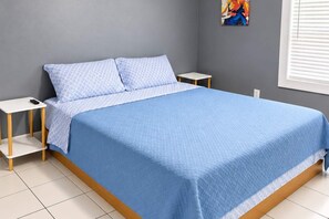 A bed with a blue quilt, two bedside tables, and a wall with a painting.
