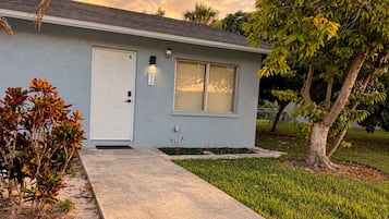 A single-story house with a front door, a garage door, and a small front yard with a tree and a shrub.