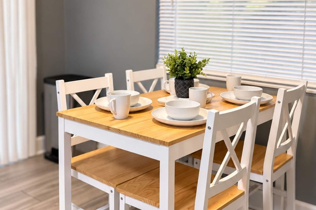 A dining table with white chairs, white plates, and a small potted plant.