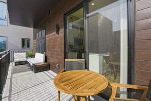 A modern outdoor patio with a wooden table and chairs, a sofa, and a small potted plant. - Penn 202| Queen Suite with Free parking + Sauna! (Pittsburgh)