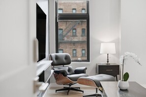 A modern office space with a desk, two leather chairs, a lamp, a small plant, and a window with a view of a brick building. - Penn 202| Queen Suite with Free parking + Sauna! (Pittsburgh)