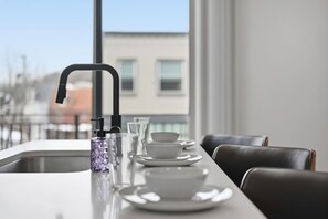 A modern dining area with a long table, black chairs, and a window with a view of buildings. - Penn 202| Queen Suite with Free parking + Sauna! (Pittsburgh)